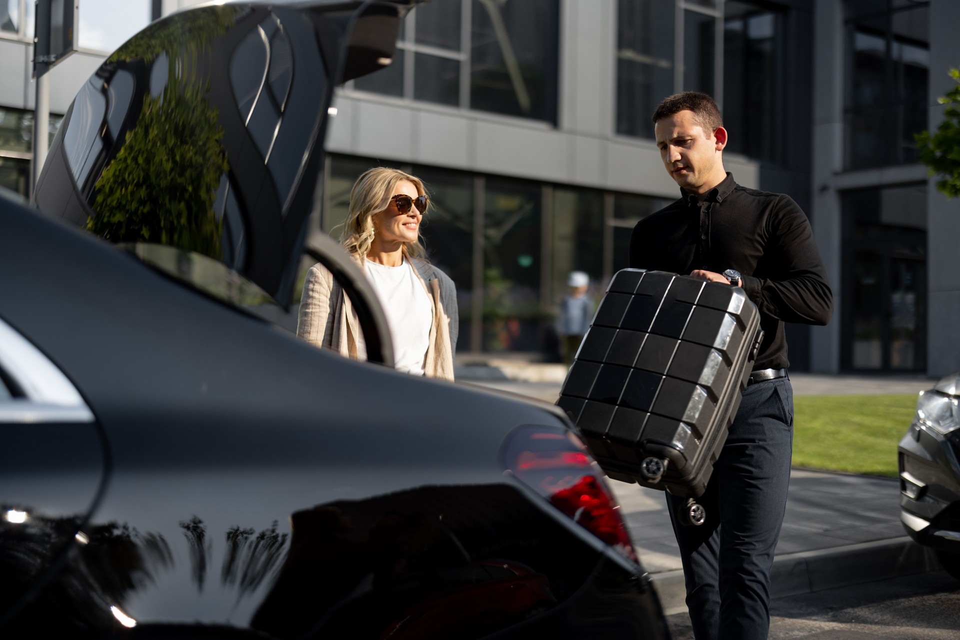 Businesswoman waits while chauffeur packs a suitcase in car trunk